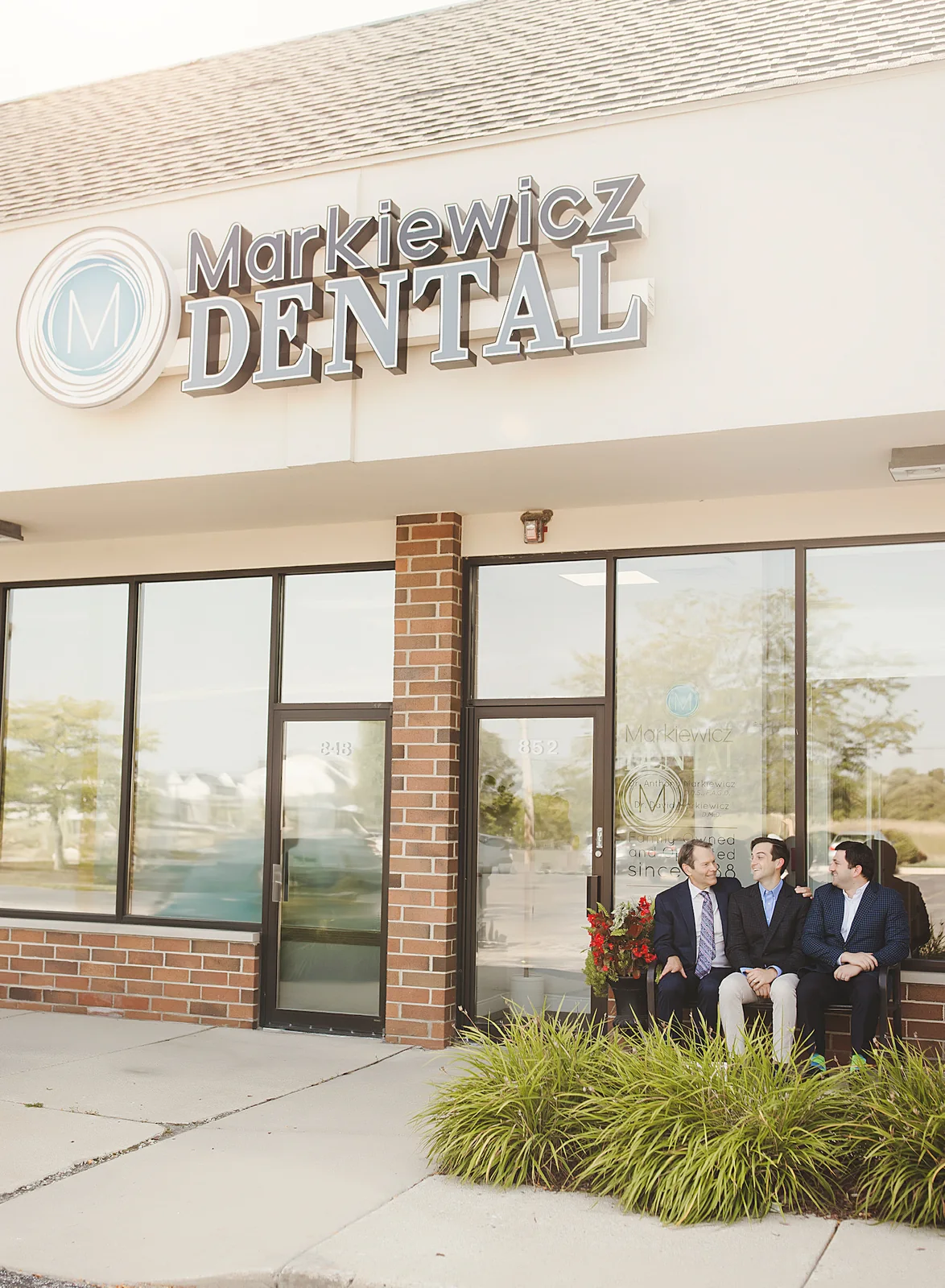 The Markiewicz Dental storefront in Mundelein, with Dr. Anthony, Dr. David, and Dr. Bogard sitting on the bench outside the entrance