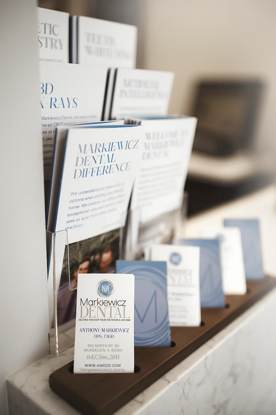 Markiewicz Dental patient brochures and business cards arranged on the front desk, including the practice's welcome guide and its 3D X-rays and Markiewicz Dental Difference leaflets