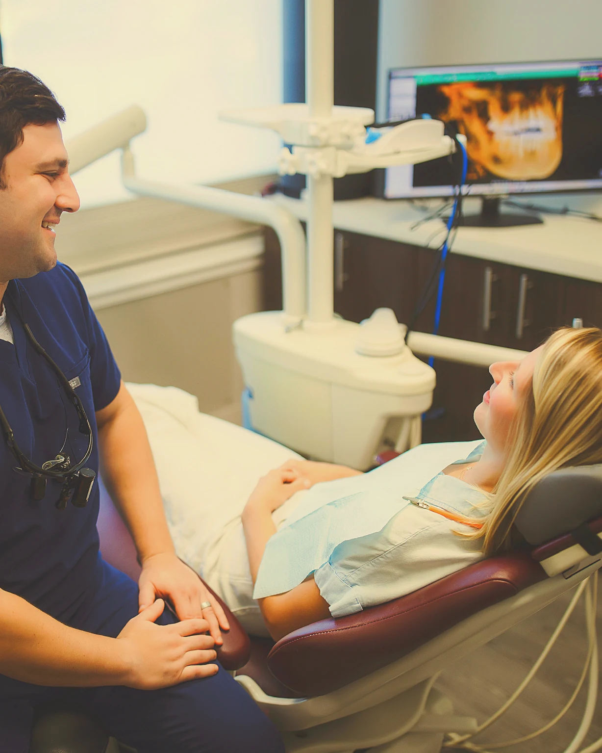 Dr. Ryan Bogard talking with a patient in the treatment chair, her CBCT scan on the monitor behind them